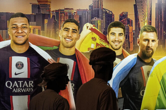 In Doha, passers-by stroll past a sign displaying PSG players competing in the 2022 World Cup, including Kylian Mbappé and Lionel Messi.