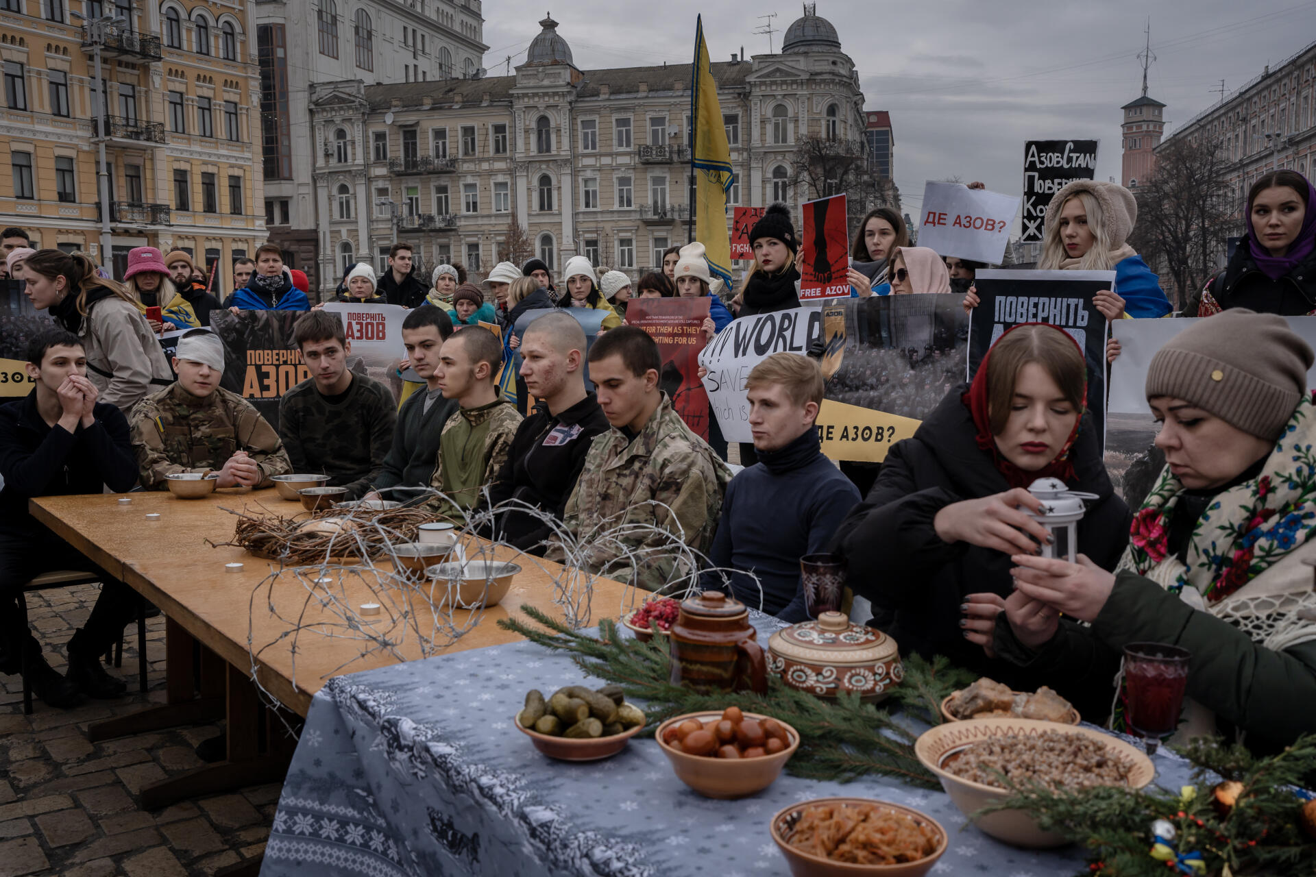 Des soldats se retrouvent face à une table vide alors que des femmes fêtent normalement Noël, lors d’une performance réalisée afin d'attirer l'attention sur la captivité des prisonners d'Azovstal, qui continue pendant les fêtes. Sur la place Sophia, à Kiev, le 24 décembre 2022. 