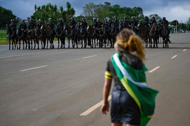 A protester watches as police troops ride horses as soldiers dismantle a camp for supporters of far-right former Brazilian President Jair Bolsonaro that had been set up outside army headquarters in Brasilia on January 9, 2023.