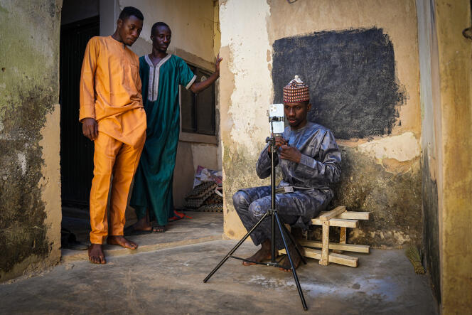 Mubarak Muhammad, también conocido como Unique Pikin, configura su teléfono para grabar un video en el patio de su casa en la ciudad de Kano, mientras sus dos hermanos observan, en diciembre de 2022.