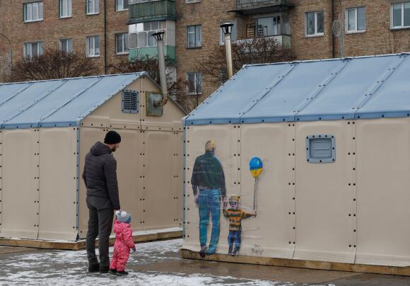 Un homme accompagné d’un enfant regarde une œuvre urbaine, dans la ville de Boutcha, près de Kiev, le 29 janvier 2023.