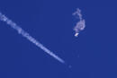In this photo provided by Chad Fish, the remnants of a large balloon drift above the Atlantic Ocean, just off the coast of South Carolina, with a fighter jet and its contrail seen below it, Feb. 4, 2023. China said Tuesday, Feb. 7, 2023, it will “resolutely safeguard its legitimate rights and interests” over the shooting down of a suspected Chinese spy balloon by the United States, as relations between the two countries deteriorate further. (Chad Fish via AP, File)