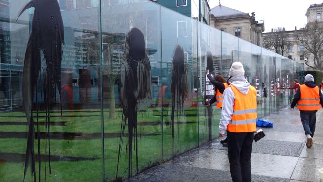 Des militants pour le climat aspergent un liquide noir et collent des affiches sur un monument sur lequel sont inscrits les articles de la Constitution allemande, à Berlin, le 4 mars 2023.