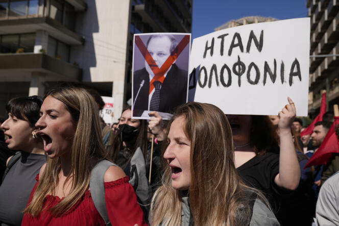 Des manifestants crient des slogans alors qu’ils tiennent une pancarte sur laquelle on peut lire en grec « C’était un meurtre » et, à droite, un portrait de l’ancien ministre des Transports Kostas Karamanlis, lors d’une manifestation en faveur des victimes d’une catastrophe ferroviaire, dans le centre d’Athènes, le mercredi 8 mars 2023.