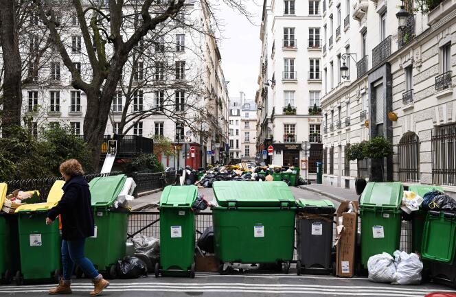 A person walks next to full trash cans, arranged in a Parisian street, March 12, 2023.