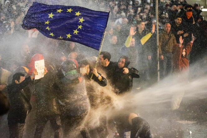 Des manifestants brandissant un drapeau de l’Union européenne s’arc-boutent alors qu’ils sont aspergés par un canon à eau lors d’affrontements avec la police anti-émeute près du Parlement géorgien, à Tbilissi, le 7 mars 2023.