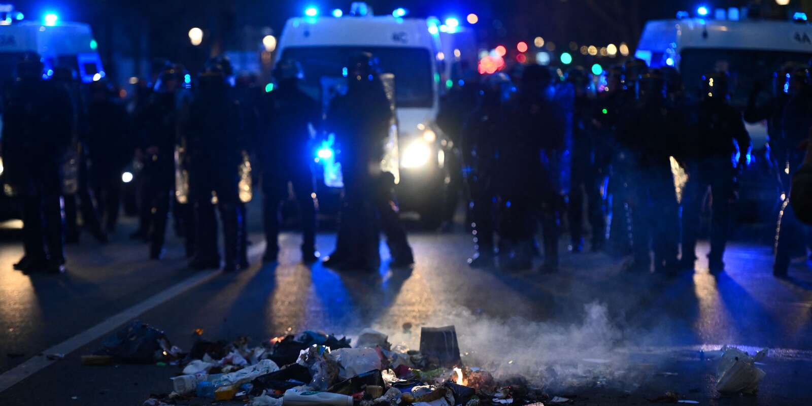 Des ordures brûlent devant la police française lors d’une manifestation contre la réforme des retraites, sur la place Vauban à Paris, le 20 mars 2023.