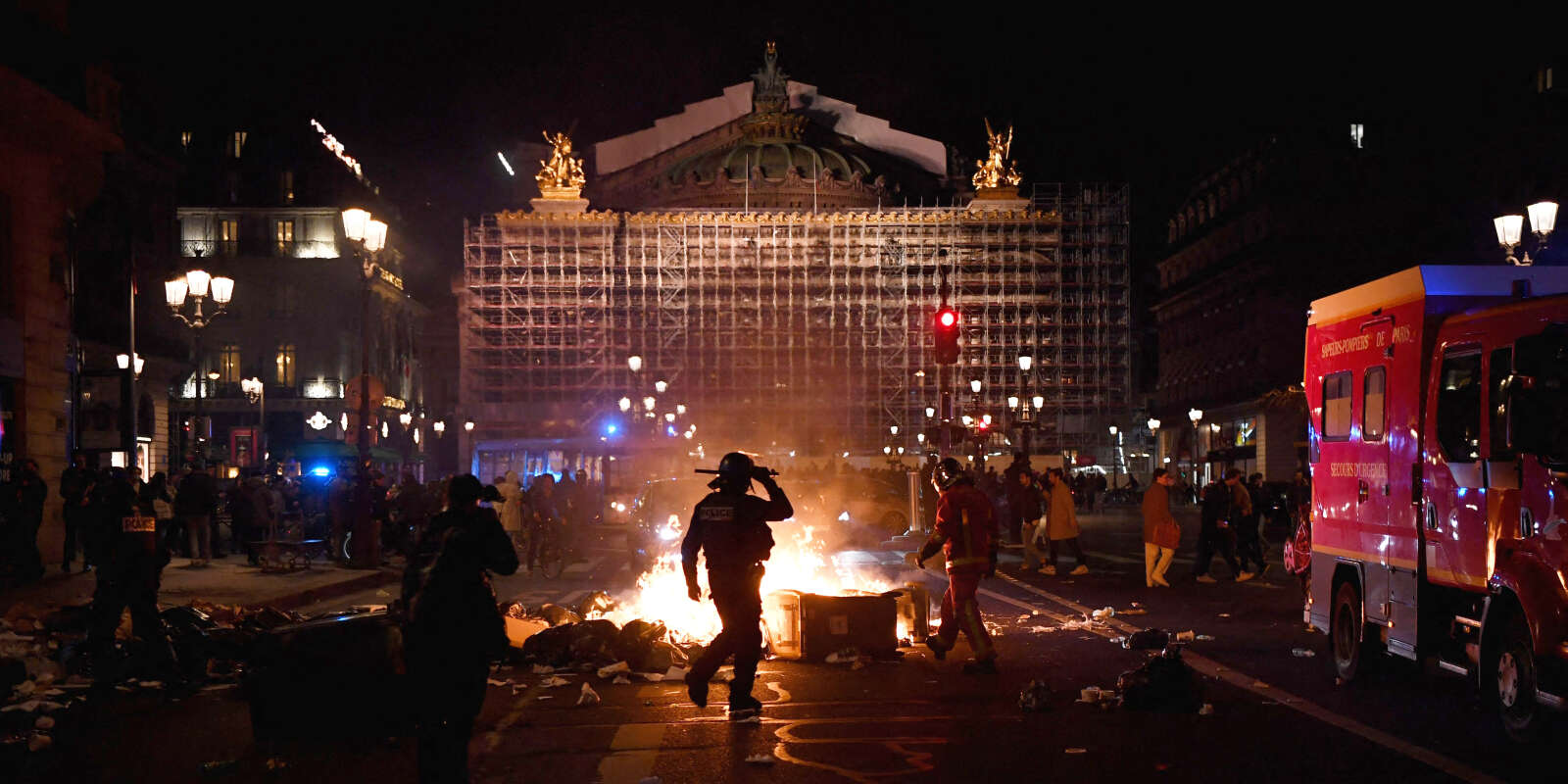 Des policiers et des pompiers se tiennent à côté d’un tas d’ordures en feu sur la place de l’Opéra, lors d’une manifestation contre le recours à utilisation l’article 49,3 pour faire passer la réforme des retraites. Paris, le 20 mars 2023. 