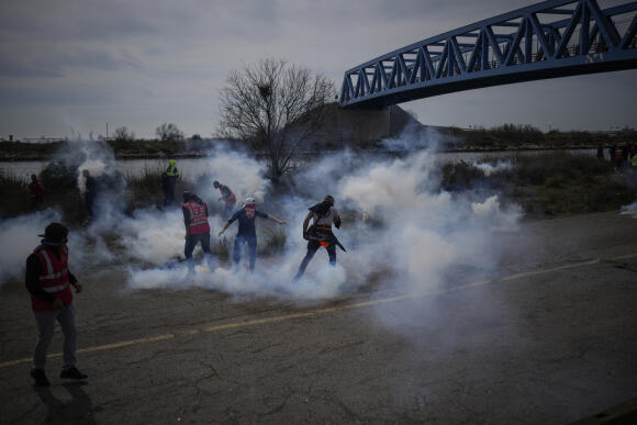 Des travailleurs de l’industrie pétrolière se tiennent au milieu des tir de gaz lacrymogène alors qu’ils bloquent l’accès au dépôt de Fos-sur-Mer, mardi 21 mars 2023.