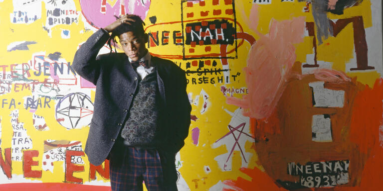 American artist, musician and producer of Haitian and Puerto Rican origins Jean-Michel Basquiat, in front of one of his paintings, during an exhibition at the Yvon Lambert gallery in Paris. (Photo by)