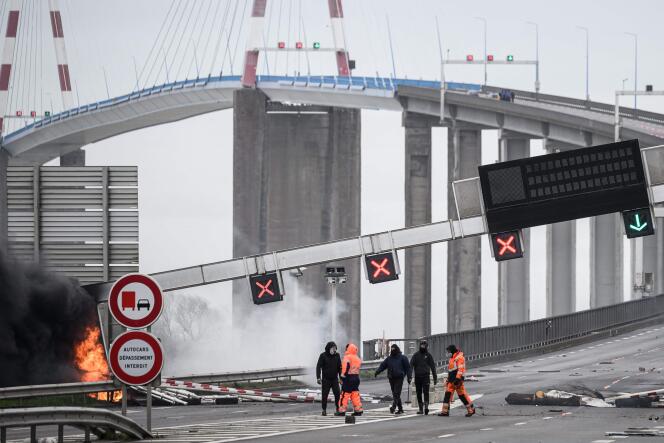 Des manifestants, mobilisés à l’entrée de Saint-Nazaire (Loire-Atlantique) contre la réforme des retraites et le 49.3, se tiennent en dessous d’un portique routier endommagé, le mercredi 22 mars 2023.