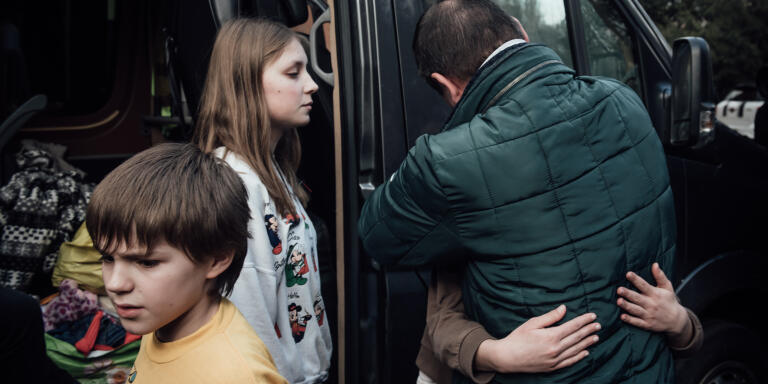 Tandis que Denys embrasse sa fille cadette, Nikita 10 ans et Dyana, 14 ans sortent du minibus qui vient de les déposer à Kiev.  Kiev, le 22 mars 2023.