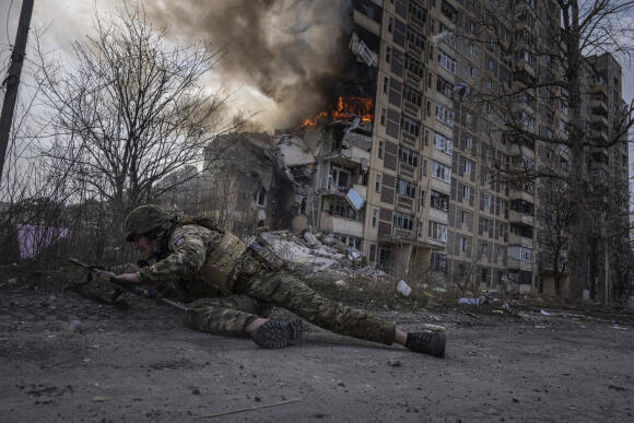 Un policier ukrainien s’abrite devant un bâtiment en feu après une frappe aérienne russe à Avdiivka, Ukraine, vendredi 17 mars 2023.(AP Photo/Evgeniy Maloletka)