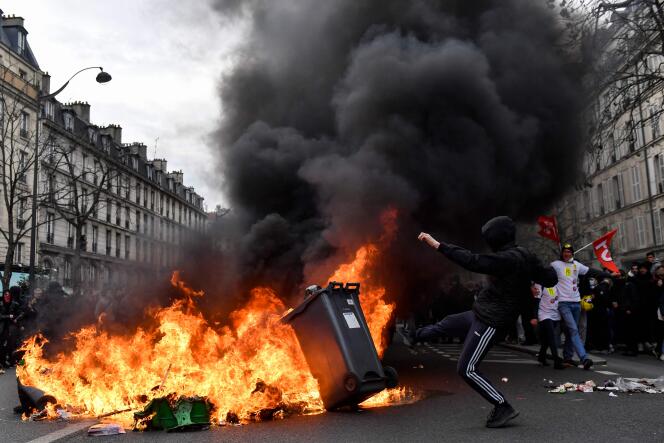 A protester kicks a bin into a fire during a demonstration after the government pushed a pensions reform through parliament without a vote, in Paris on March 28, 2023. 