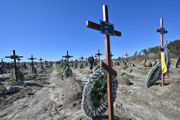 Un homme marche parmi les tombes de personnes non identifiées qui ont été tuées dans la ville ukrainienne de Boutcha, au nord-ouest de Kiev, le 30 mars 2023.