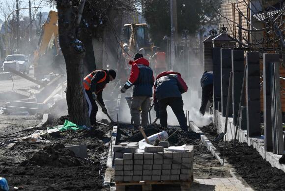Des ouvriers effectuent des travaux de réparation dans la rue Vokzalna dans la ville ukrainienne de Boutcha, au nord-ouest de Kiev, le 30 mars 2023, là où une colonne blindée russe a été détruite.