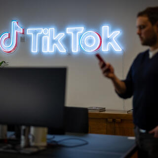An employee looks at his mobile phone as he walks past the logo of the video-focused social networking service TikTok, at the TikTok UK offices, in London, on February 9, 2022. - With a billion users, TikTok has rapidly become one of the most important players in the music industry, and now has its sights set on revolutionising the way artists are discovered and get paid. (Photo by Tolga Akmen / AFP)
