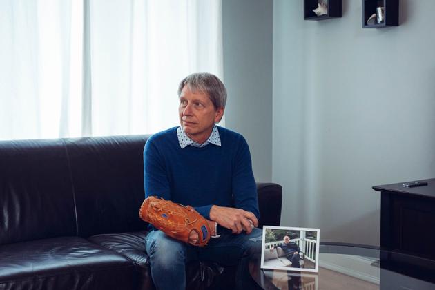 Ghyslain Poisson, chez lui, avec un gant de base-ball que son père (sur la photo) avait acheté pour échanger des balles avec son fils. A Montréal, le 23 mars 2023,.