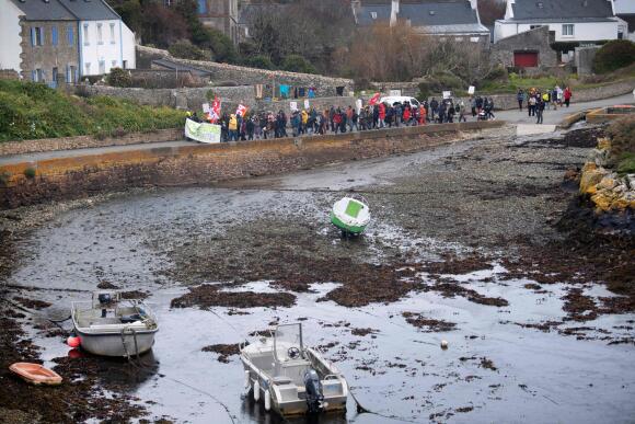 Des manifestants marchent le long d’une digue près de bateaux amarrés à marée basse, sur l’île d’Ouessant, au large de la côte bretonne, le 13 avril 2023.