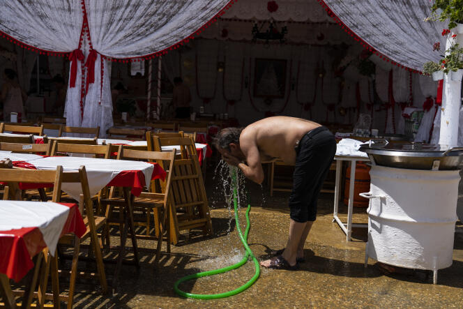 A man refreshes himself with a water hose outside a 'caseta' (tent where food and drinks are served) in the annual traditional April Fair in Seville, Spain, Thursday, April 27, 2023. 