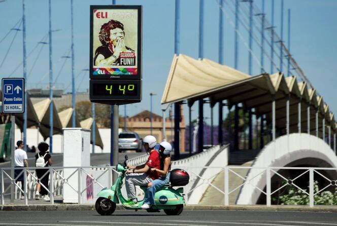 A couple ride a Vespa motorcycle past a street thermometer reading 44 degrees Celsius in Seville on April 26, 2023.
