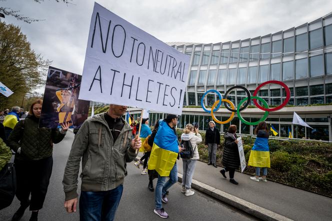 Ukrainians walk past the headquarters of the International Olympic Committee during a protest in Lausanne on March 25, 2023.