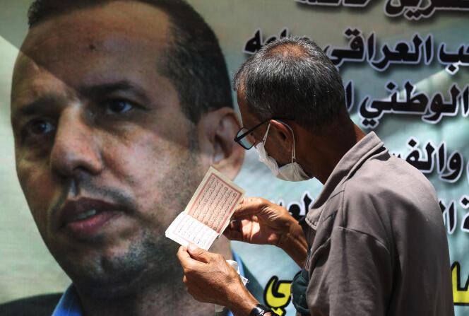 Un Irakien récite des versets du Coran devant une affiche de l’expert irakien en djihadisme Hicham Al-Hachémi, à Bagdad, en Irak, le 12 juillet 2020.