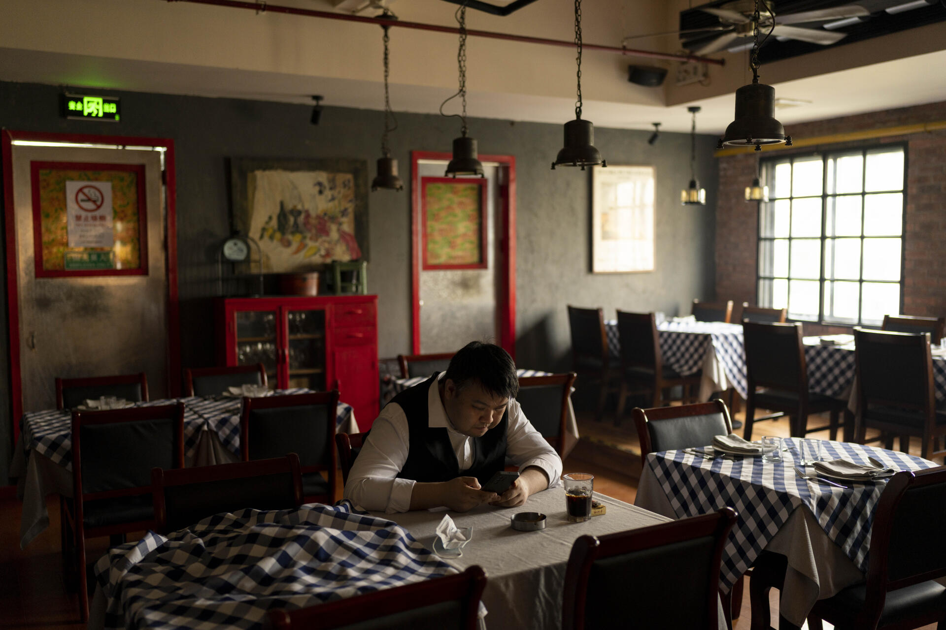 A waiter browses on his smartphone at a restaurant in Shanghai on June 6, 2023.