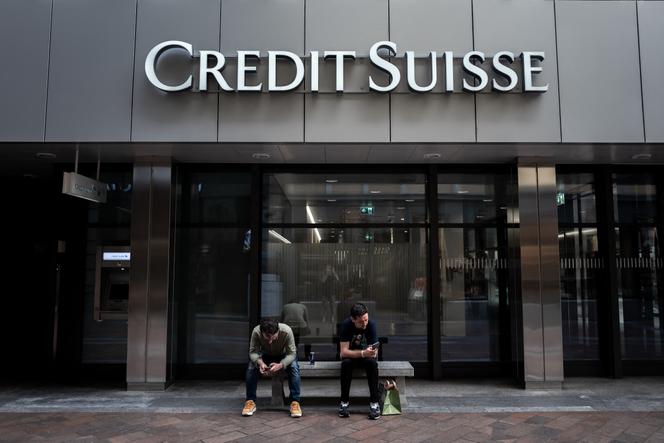 Deux hommes sont assis sous une enseigne du Credit Suisse affichée sur un immeuble à Lugano, le 9 juin 2023.