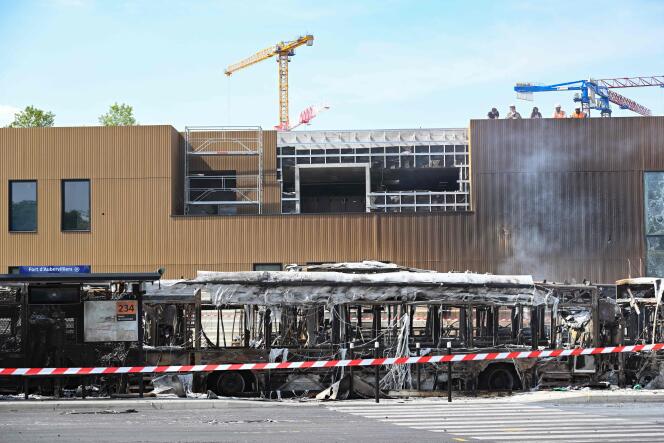 The remains of a dozen buses in Aubervilliers (outside Paris) on June 30 that were set on fire during the night at a RATP depot next to the site where the future Olympic training pool is being built (in the background).