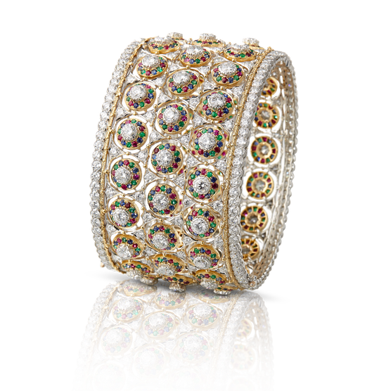 Pulsera Buccellati con elementos redondos de oro amarillo engastados alternativamente con diamantes, esmeraldas, rubíes y zafiros. En el centro, un bisel de oro blanco modelado en forma de hoja y engastado con diamantes. Brillantes perlas de oro amarillo y secciones de oro amarillo, modeladas en hojas sucesivas, separan la banda central de las orlas de oro blanco y diamantes.