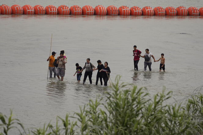 Migrantes cruzan el Río Grande mientras se instala una barrera flotante en Eagle Pass, Texas, el 12 de julio de 2023.