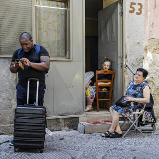 07 July 2023, Naples, Italy - A tourist with his luggage, observed by two women inhabitants of the Spanish Quarters.