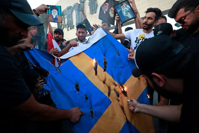 Des manifestants brûlent un drapeau suédois sur la place Tahrir à Bagdad, à la suite du piétinement d’un coran à Stockholm, le 20 juillet 2023.