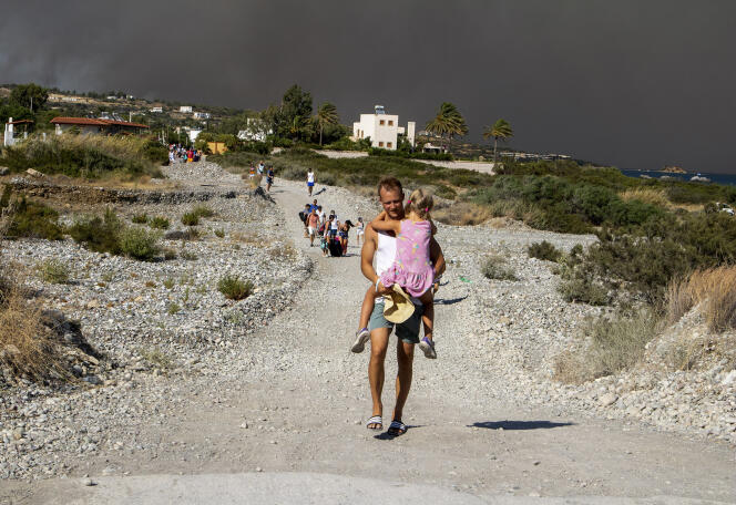 Un homme porte son enfant et quitte une zone en proie aux incendies, sur l’ile de Rhodes, en Grèce, le 22 juillet 2023. 