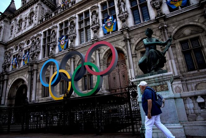A man walks past the Olympic rings in front of the Paris City Hall one year until the Paris 2024 Olympic Games opening ceremony, Wednesday, July 26, 2023. (AP Photo/Christophe Ena)