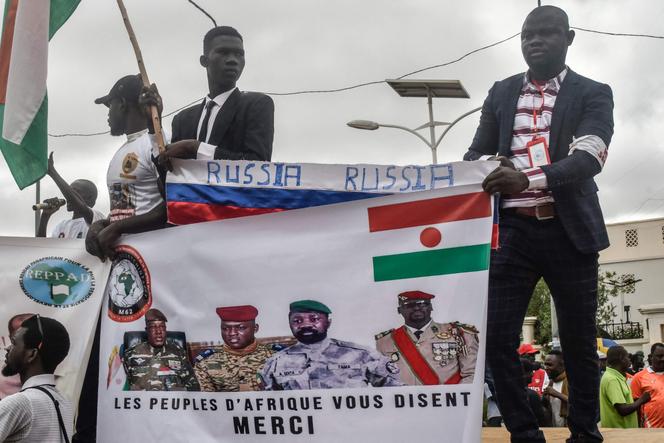 Protesters hold a Russian flag and a banner with images of (from L to R): General Abdourahamane Tiani, Niger’s new strongman, Burkina Faso's junta leader Captain Ibrahim Traore, leader of Mali's junta, Assimi Goita, and Guinea's junta leader, Colonel Mamady Doumbouya, during a demonstration on independence day in Niamey on August 3, 2023. 