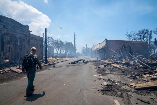 In this photo provided by Tiffany Kidder Winn, a man walks past wildfire wreckage on Wednesday, August 9, 2023, in Lahaina, Hawaii.