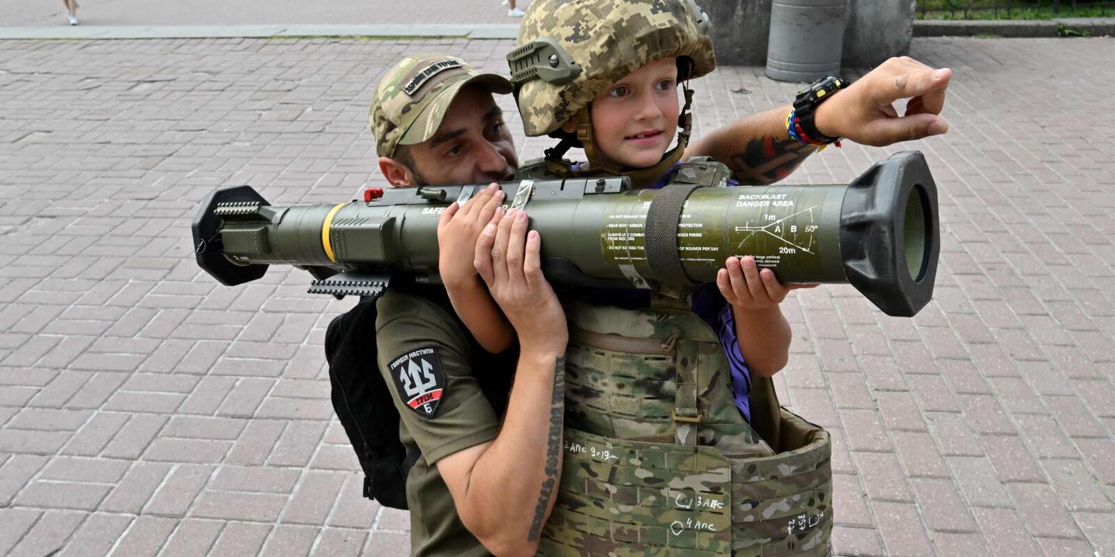 Un militaire ukrainien aide un garçon à tenir une arme antichar sur un point de volontaires au centre de Kiev le 10 août 2023.
