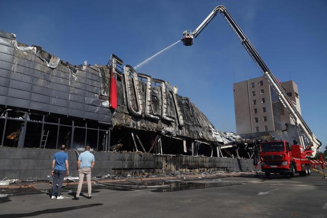 Employees look at the rescuers spraying water on the burnt out structure of a supermarket destroyed as a result of night strike in Odesa on August 14, 2023.
