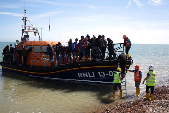 Members of Royal National Lifeboat Institution help migrants to disembark from a Royal National Lifeboat Institution (RNLI) lifeboat on the beach at Dungeness, on the southeast coast of England, on August 16, 2023, after being picked up at sea while crossing the English Channel from France.