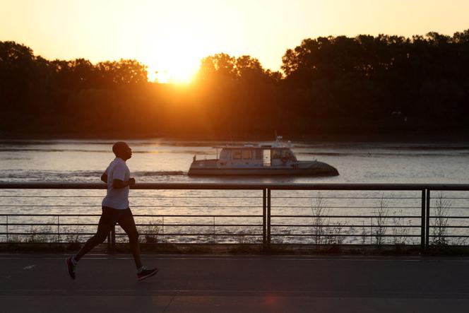 A man jogs along the docks at sunrise to avoid the heat, in Bordeaux, southwestern France, on August 21, 2023. 