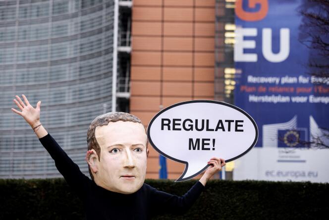 Un militant de l’ONG environnementale Avaaz portant un masque représentant le PDG de Meta, Mark Zuckerberg, tient une banderole sur laquelle est écrit « Régulez-moi », lors d’une action marquant la publication de la loi sur les services numériques, devant le bâtiment de la Commission européenne, à Bruxelles, le 15 décembre 2020.