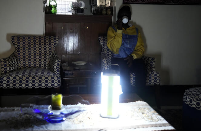 Una mujer keniana bebe una taza de té, iluminada por una lámpara de emergencia, el sábado 26 de agosto de 2023.