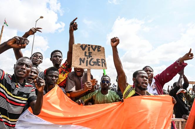 Supporters of the Niger's National Council for the Safeguard of the Homeland (CNSP) wave a placard as they demonstrate outside the Niger and French airbases in Niamey on August 27, 2023. 