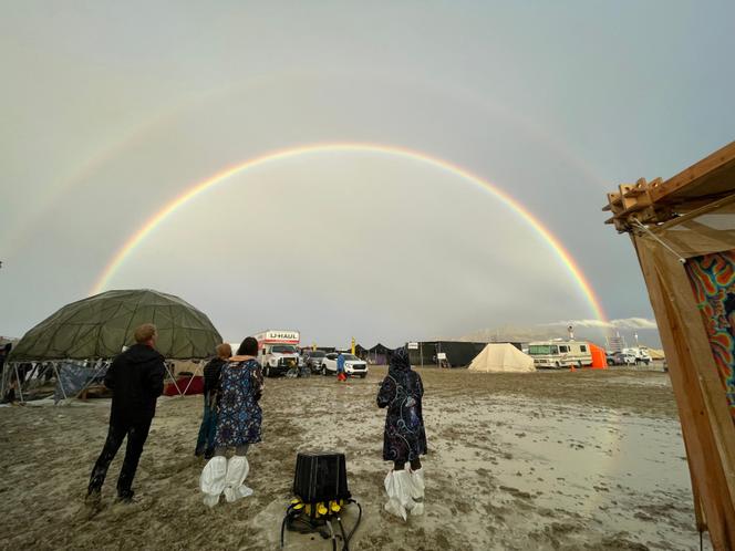 Attendees look at a double rainbow over flooding on a desert plain on September 1, 2023, after heavy rains turned the annual Burning Man festival site in Nevada's Black Rock desert into a mud pit.