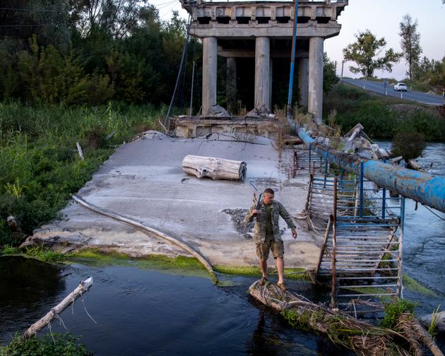 A fisherman uses a log to cross the Siverskyi Donets River, which flows through Izium, Ukraine, on September 12, 2023.