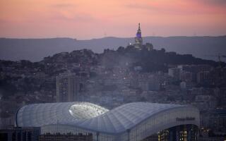 (FILES) This photograph taken in Marseille, southern France, on October 17, 2021 shows the Velodrome stadium and 'Notre Dame de la Garde' cathedral at dawn. Marseille, where Pope Francis is expected on Friday, is one of the great ports of the Mediterranean, shaped since its foundation by waves of migrations and where communities and religions cohabit. Two key themes of this visit. (Photo by Nicolas TUCAT / AFP)