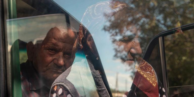 ERIC GRIGORIAN FOR LE MONDE Yenok Aghajanyan, 78, and his wife Elanora, 78, (reflected in the car window) wait for help to transport their broken car in the village of Kornidzor, Armenia, a border village, on Sept. 27, 2023. From the town of Askeran in Nagorno-Karabakh, the two had just arrived into Armenia.