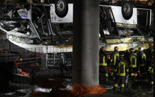 Italian firefighters work at the scene of a passenger bus accident in Mestre, near Venice, Italy, Wednesday, Oct. 4, 2023. According to local media, the bus fell a few meters from an elevated rod before crashing Tuesday close to Mestre's railway tracks, where it caught fire. (AP Photo/Antonio Calanni)